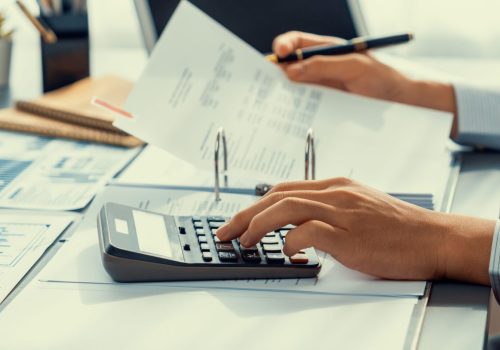 Corporate auditor calculating budget with calculator on his office desk. Dedicated accountant professional of accounting business company analyzing financial document to forecast income. Insight